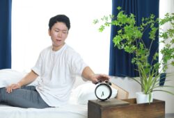 不機嫌な顔で目覚ましを止める男性